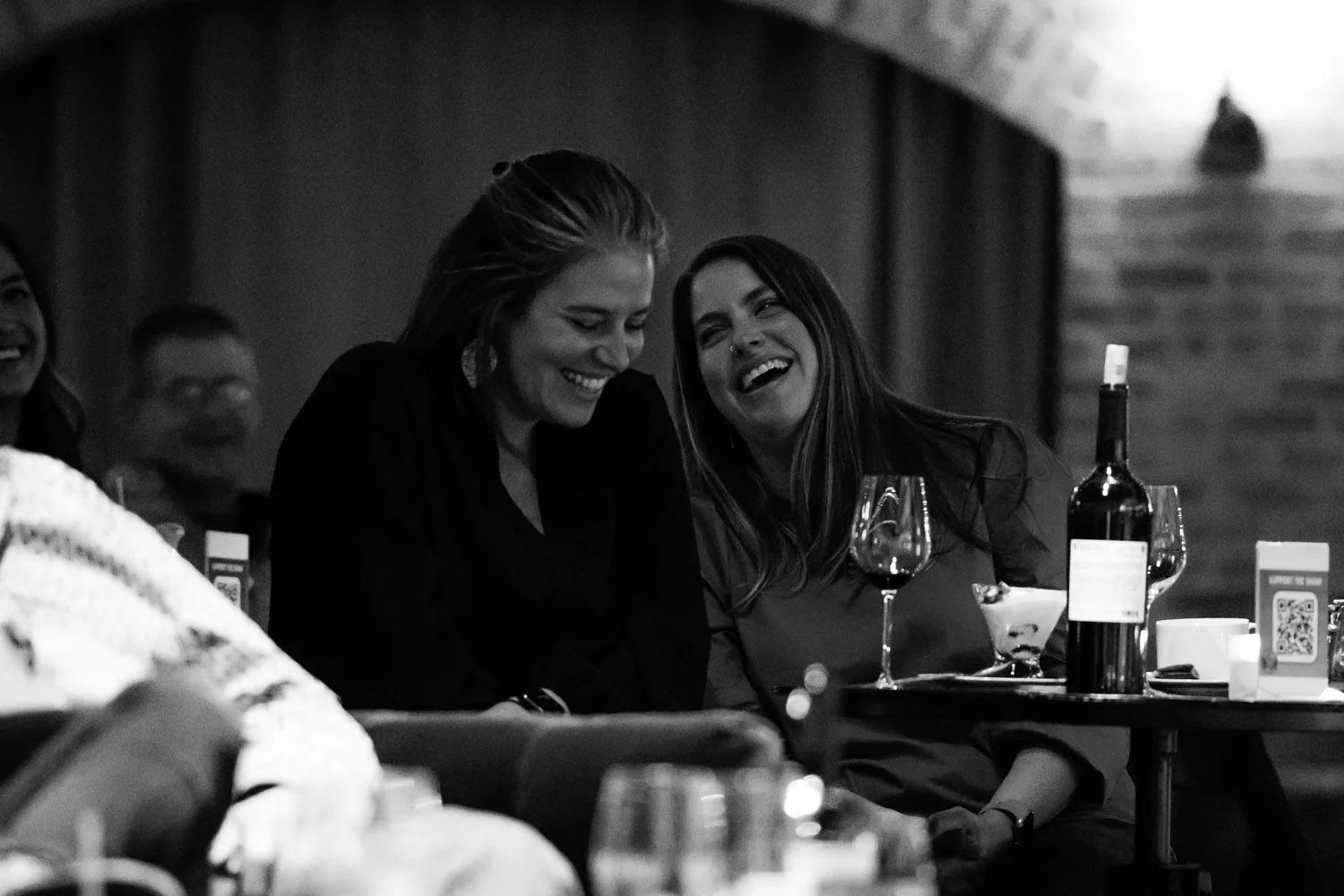 Two friends laughing at their table next to a bottle of wine